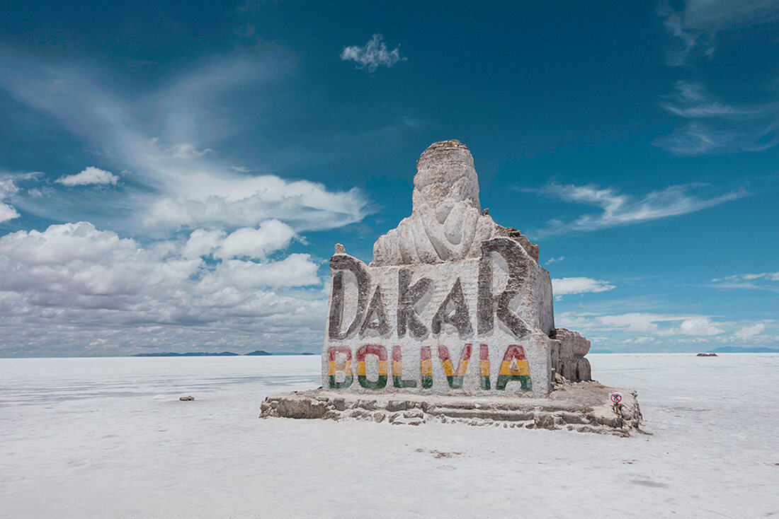 Large rock sign of Dakar Bolivia in the salt flats below a blue sky with white clouds.