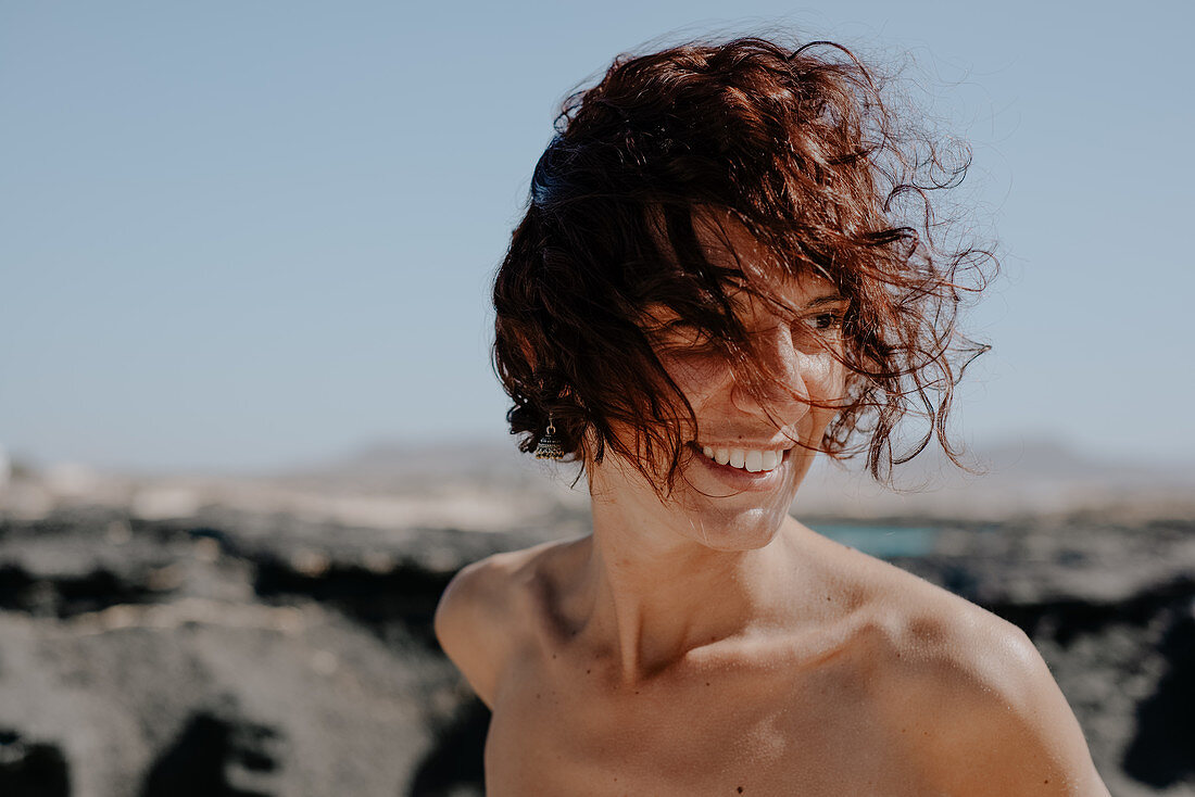 Kopf und Schultern Porträt der lächelnden Frau mit braunem lockigem Haar auf Fuerteventura.