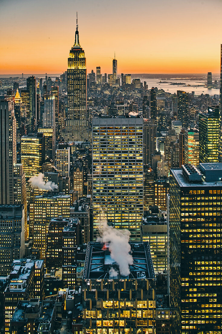 View of Manhattan skyline with illuminated skyscrapers at sunset, New York City