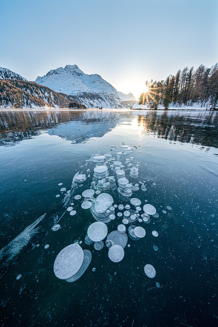 Ice bubbles trapped in frozen Lake Sils at sunset with Piz Da La Margna in background, Engadine, Graubunden canton, Switzerland, Europe