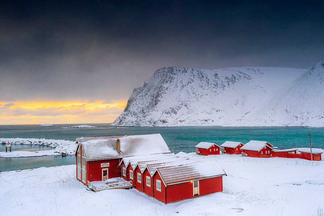 Wintersonnenuntergang über dem arktischen Meer und Fischerhütten im Schnee, Sorvaer, Soroya-Insel, Hasvik, Troms og Finnmark, Norwegen, Skandinavien, Europa