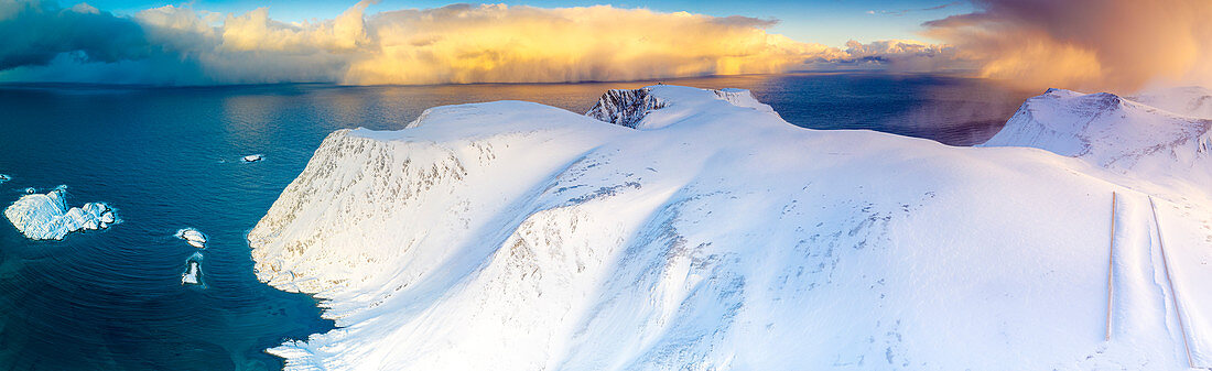Luftaufnahme des Sonnenaufgangs auf schneebedeckten Bergen und blauem arktischem Meer, Sorvaer, Soroya-Insel, Hasvik, Troms og Finnmark, Arktis, Norwegen, Skandinavien, Europa