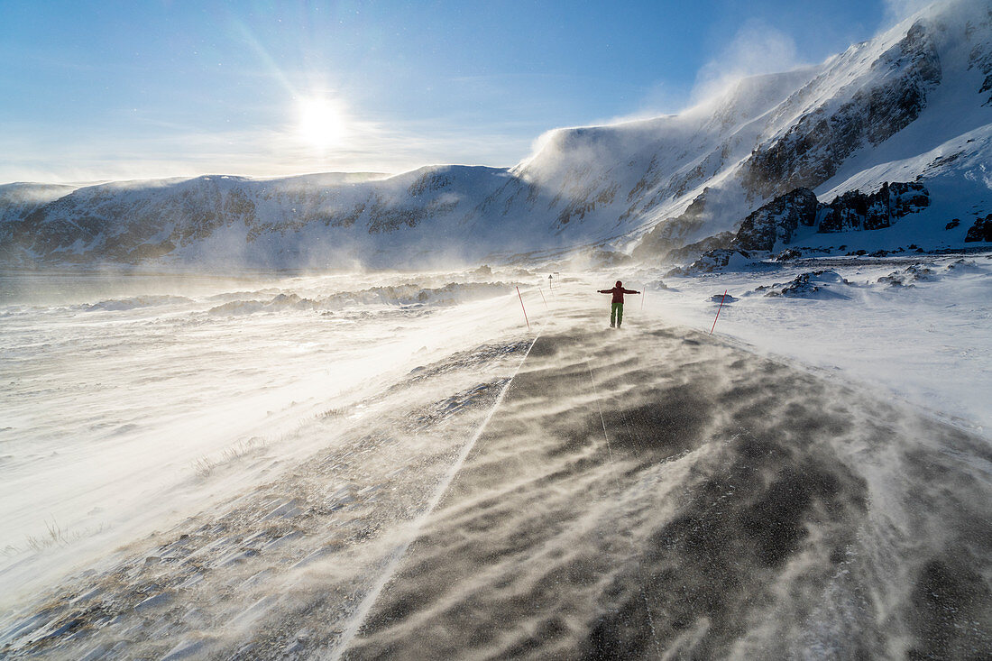 Der Mensch freut sich auf einer eisigen leeren Straße entlang der Barentssee während des arktischen Windsturms, Berlevag, Varanger-Halbinsel, Finnmark, Norwegen, Skandinavien, Europa