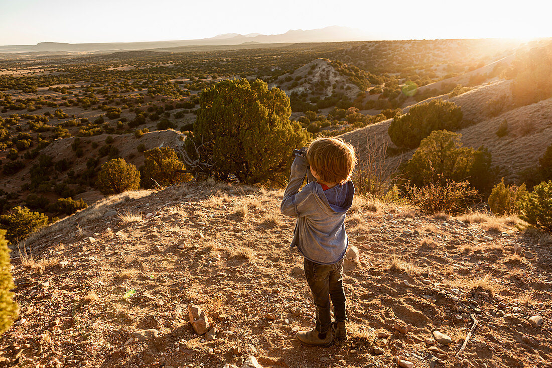 kleiner Junge im Galisteo-Becken, der durch Fernglas bei Sonnenuntergang schaut