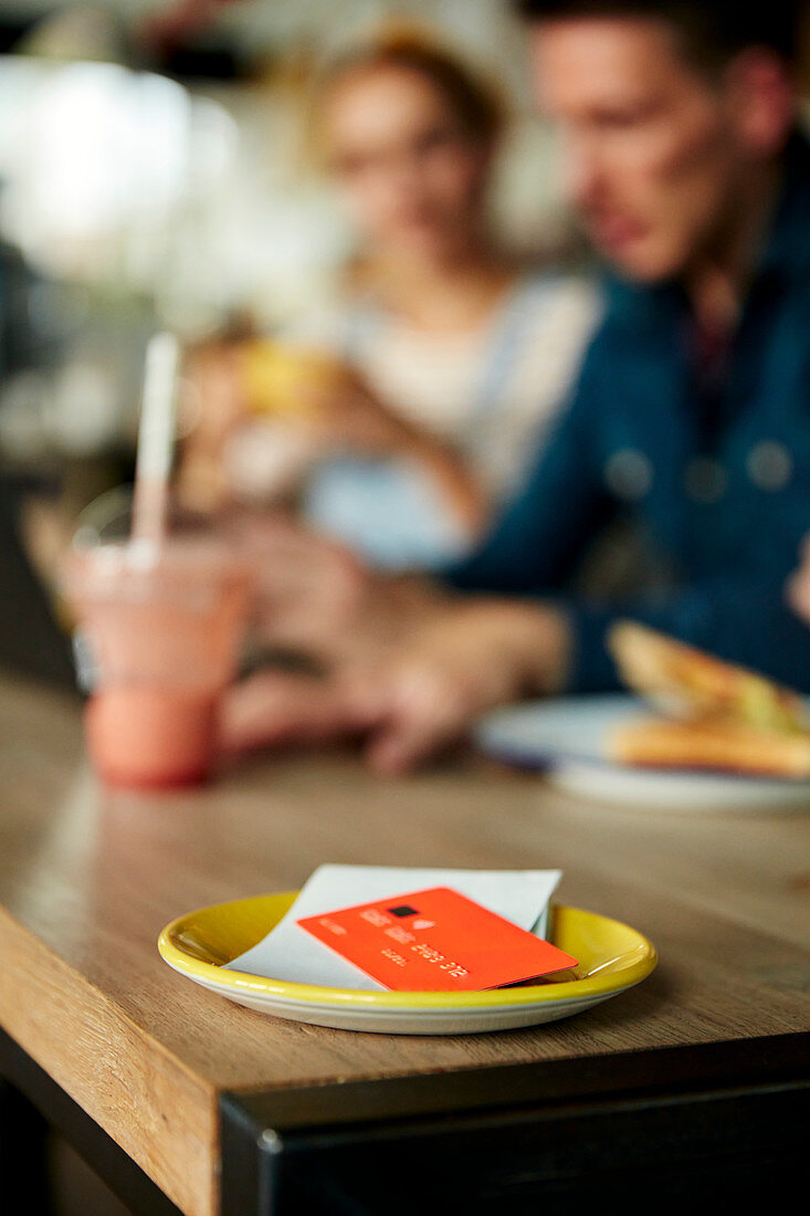 Leute an einem Cafétisch, eine Untertasse mit Kassenbeleg und Kreditkarte