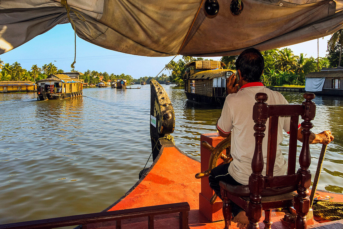 Kapitän am Telefon und Steuerung des Hausboots durch die Backwaters auf einer beliebten Backwater-Kreuzfahrt, Alappuzha (Alleppey), Kerala, Indien, Asien