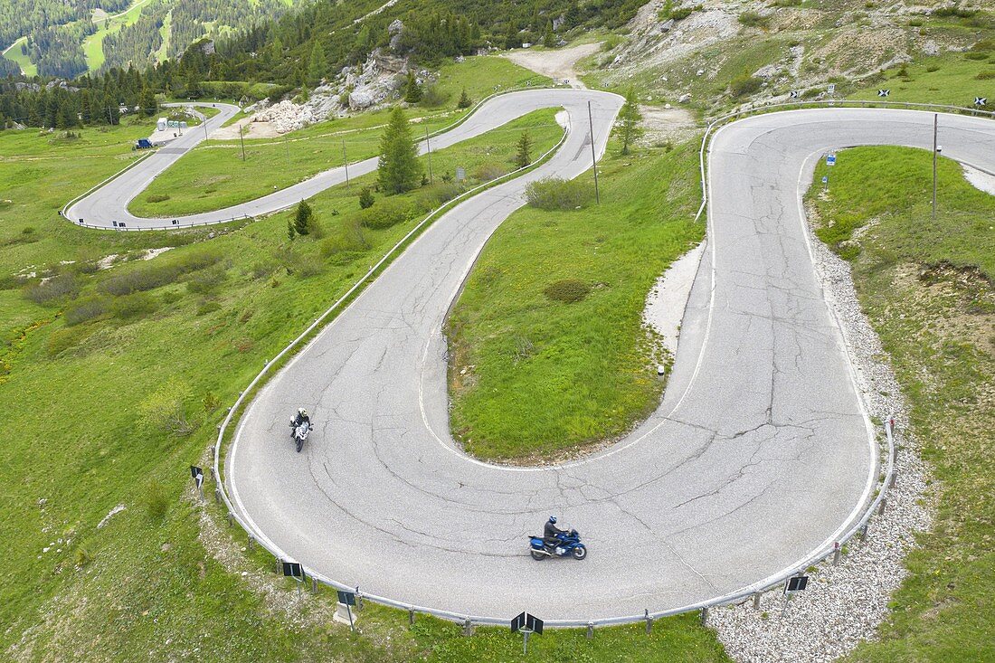 Drohnen-Luftaufnahme von zwei Motorradfahrern, die die kurvige Straße des Pordoi-Passes während eines Sommertages reisen, Fassa-Tal, Dolomiti, Gemeinde Canazei, Provinz Trento, Trentino-Südtirol, Italien, Europa