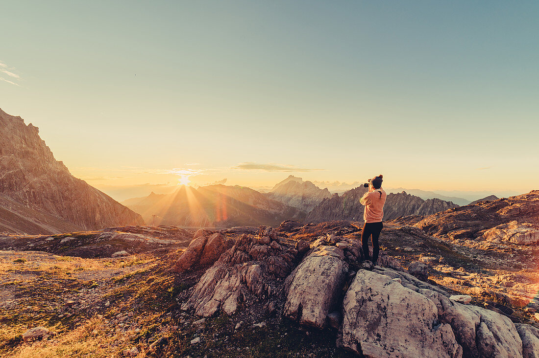 Frau mit Kamera beim Sonnenaufgang in den Bergen im Rätikon, Vorarlberg, Österreich, Europa