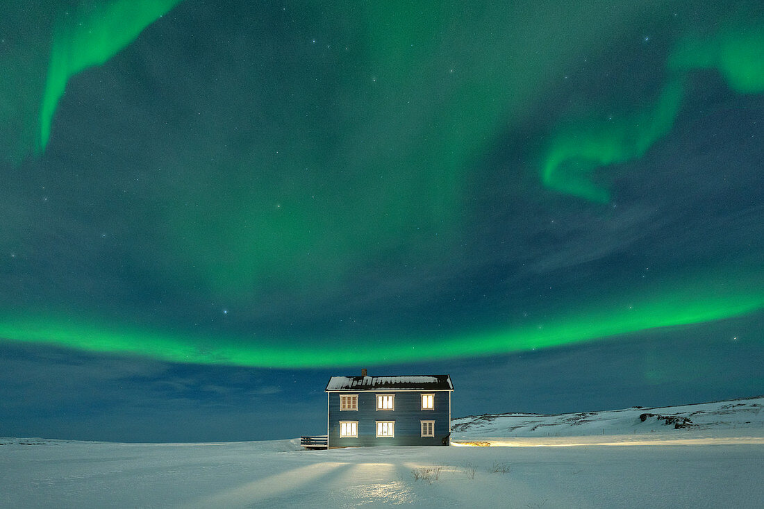 Nordlichter (Aurora borealis) auf dem beleuchteten Haus im Schnee, Adern, Kongsfjord, Halbinsel Varanger, Finnmark, Norwegen, Skandinavien, Europa
