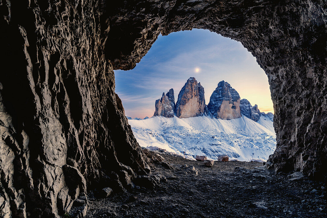 Tre Cime di Lavaredo beleuchtet vom Mond gesehen von der Öffnung in Felsen einer Kriegshöhle, Sestodolomiten, Trentino-Südtirol, Italien, Europa