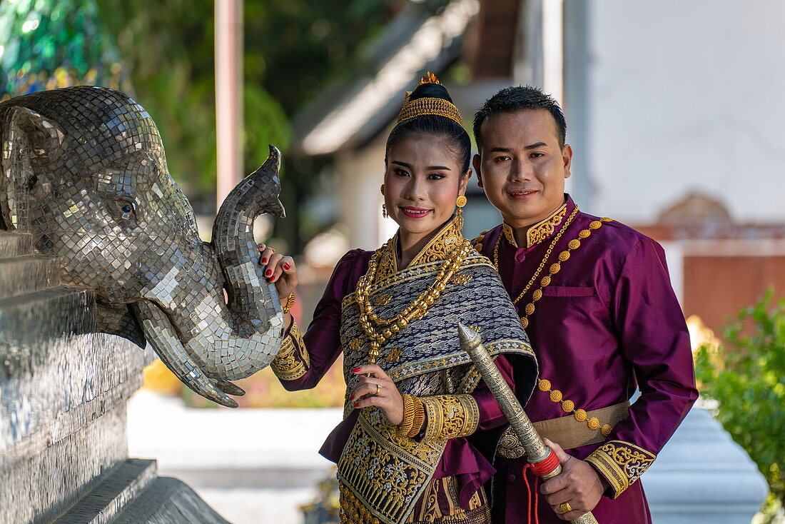 Glückliches Hochzeitspaar in herrlicher laotischer Hochzeitskleidung während Fotoshooting am Wat Xieng Thong Tempel, Luang Prabang, Provinz Luang Prabang, Laos, Asien