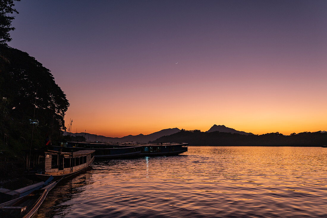 Silhouette of longtail excursion boats on Mekong river and mountains at sunset, Luang Prabang, Luang Prabang Province, Laos, Asia