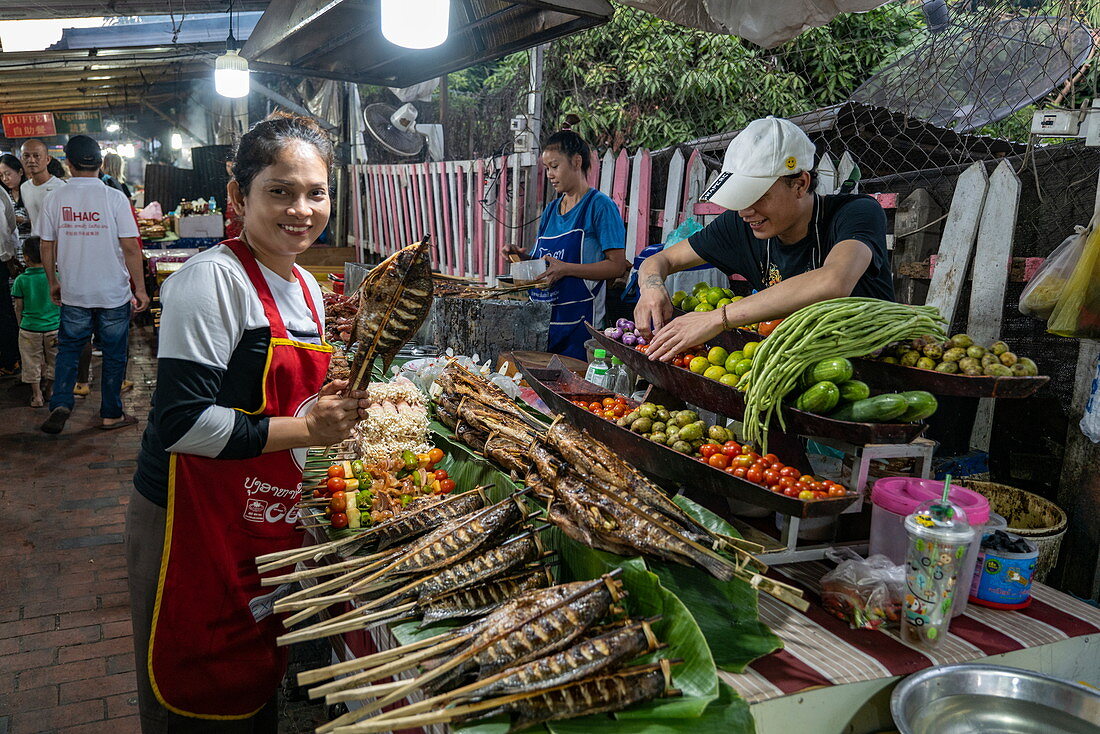 Frau präsentiert einen frisch gegrillten Fisch aus dem Mekong an einem Verkaufsstand entlang der Sisavangvong Road (der Hauptstraße), Luang Prabang, Provinz Luang Prabang, Laos, Asien