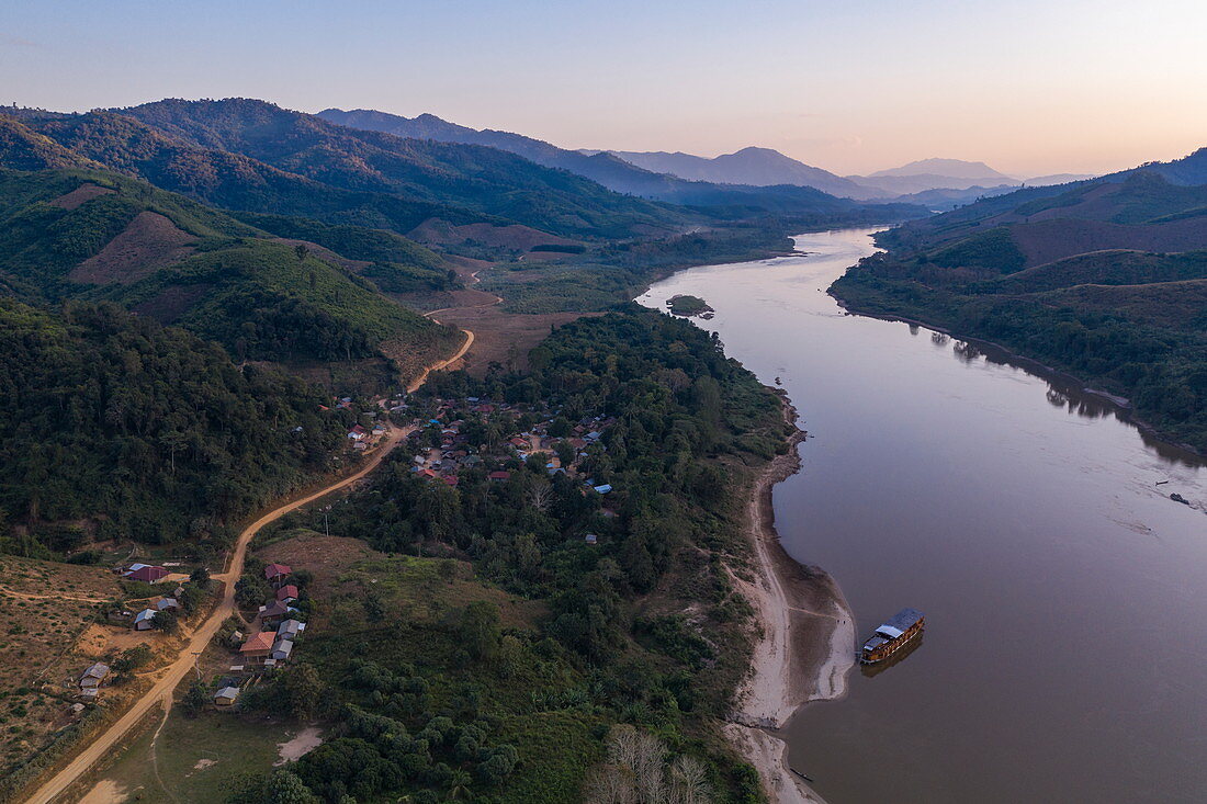 Luftaufnahme von unbefestigter Straße neben Fluss Mekong mit Bergen in der Ferne in der Abenddämmerung, Ban Hoy Palam, Bezirk Pak Tha, Provinz Bokeo, Laos, Asien