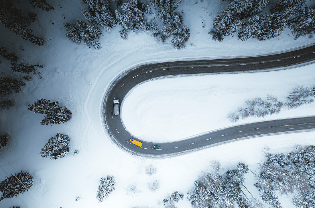 Luftaufnahme von Autos, die auf Kurven der schneebedeckten Bergstraße im Winter, Schweiz, Europa fahren