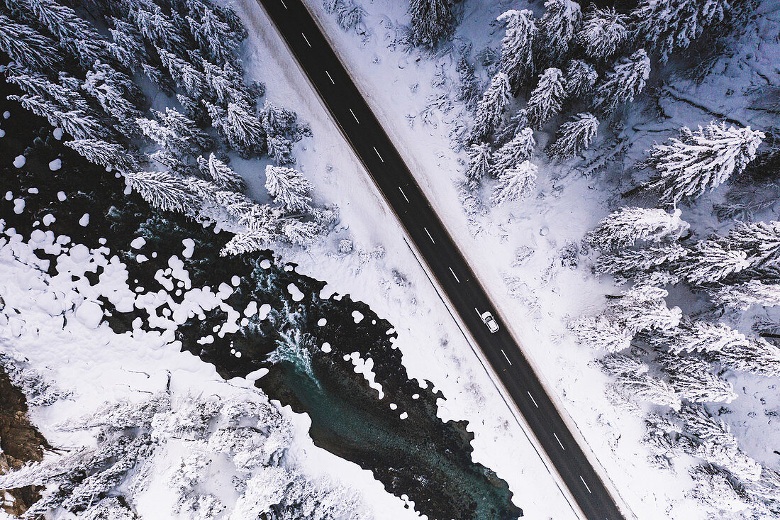 Auto, das auf schneebedeckter Bergstraße über gefrorenem Fluss und Wald, Luftbild, Schweiz, Europa reist