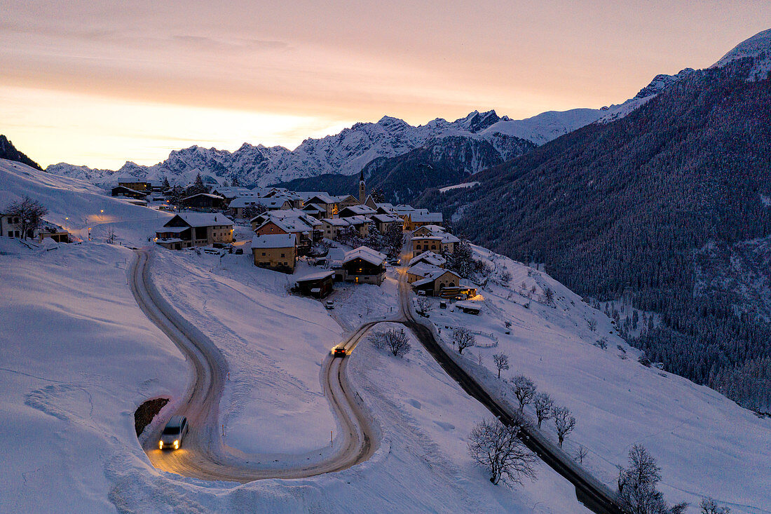 Autos fahren auf Haarnadelkurven der verschneiten Straße im Morgengrauen, Guarda, Unterengadin, Kanton Graubunden, Schweiz, Europa