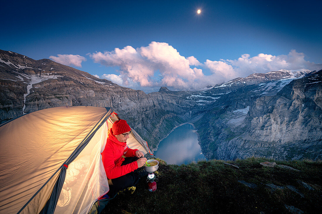Wanderer Mann mit Zelt mit Campingkocher auf Grat über See Limmernsee, Kanton Glarus, Schweiz, Europa