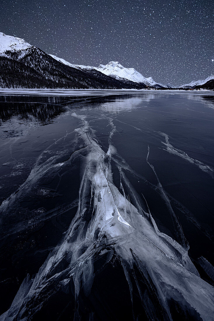 Starry night sky over the cracked ice on frozen Lake Silvaplana in winter, Maloja, Engadine, Graubunden canton, Switzerland, Europe