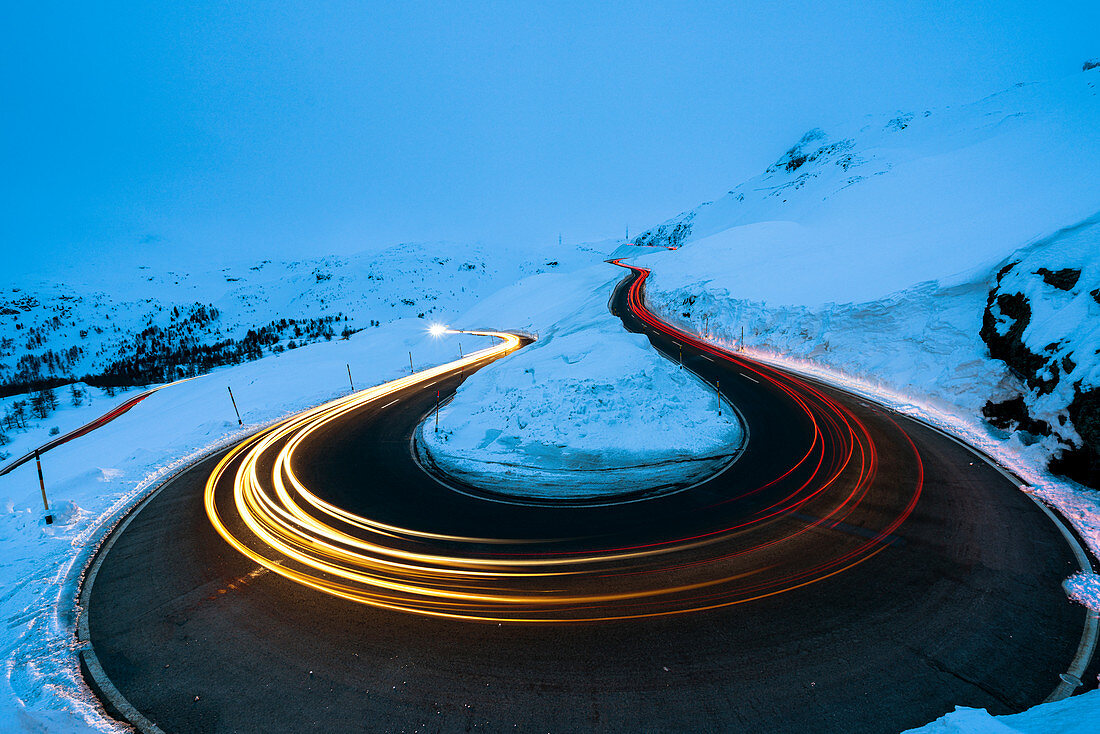Car trail lights on bends of Bernina Pass road in winter, Val Poschiavo, canton of Graubunden, Engadin, Switzerland, Europe