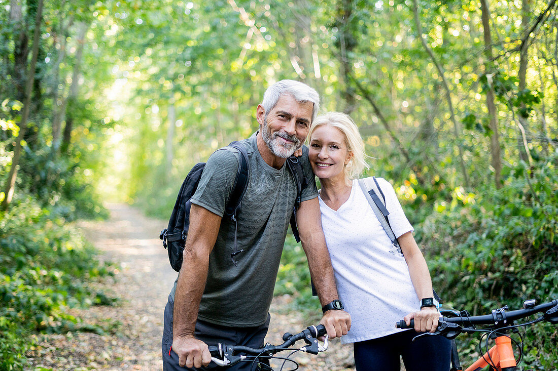 Porträt des lächelnden reifen Paares mit Fahrrädern, die im Wald stehen