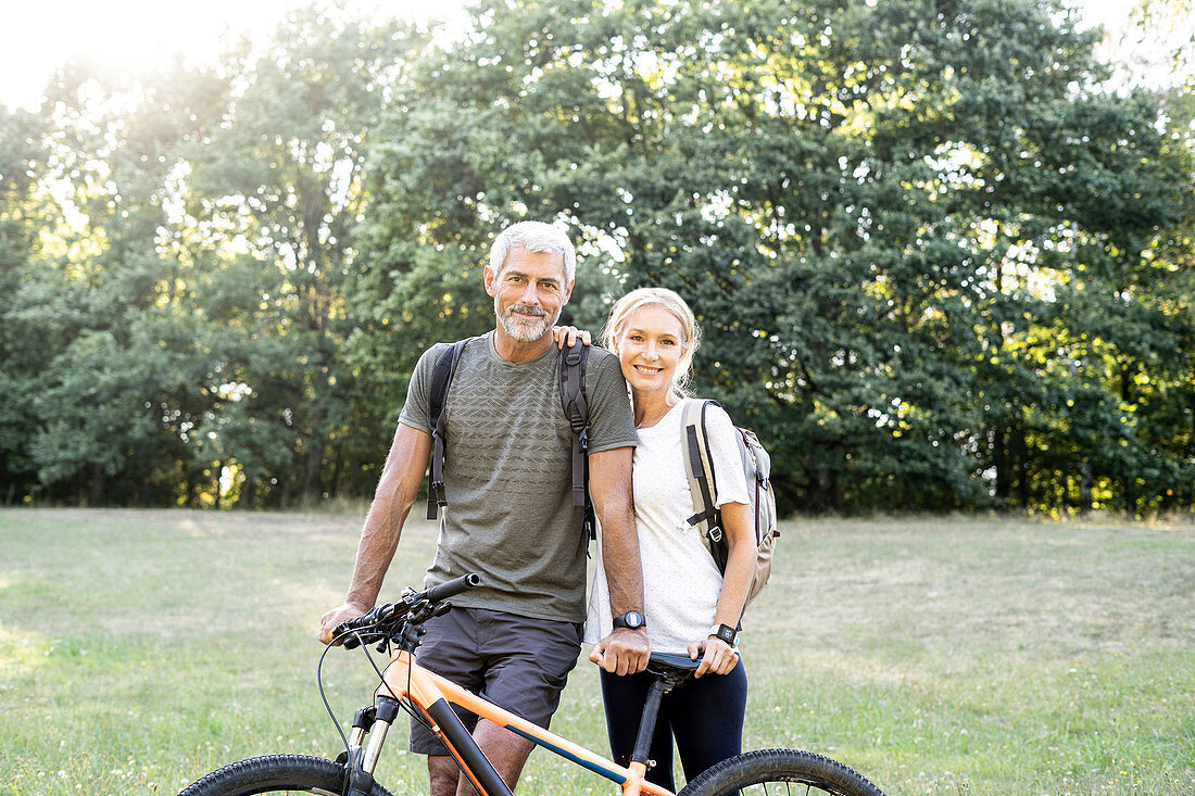 Porträt des lächelnden reifen Paares mit dem Fahrrad, das im Wald steht
