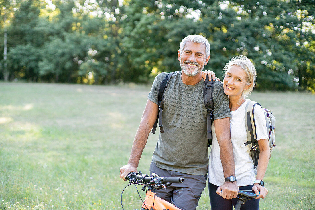 Porträt des lächelnden reifen Paares mit dem Fahrrad, das im Wald steht