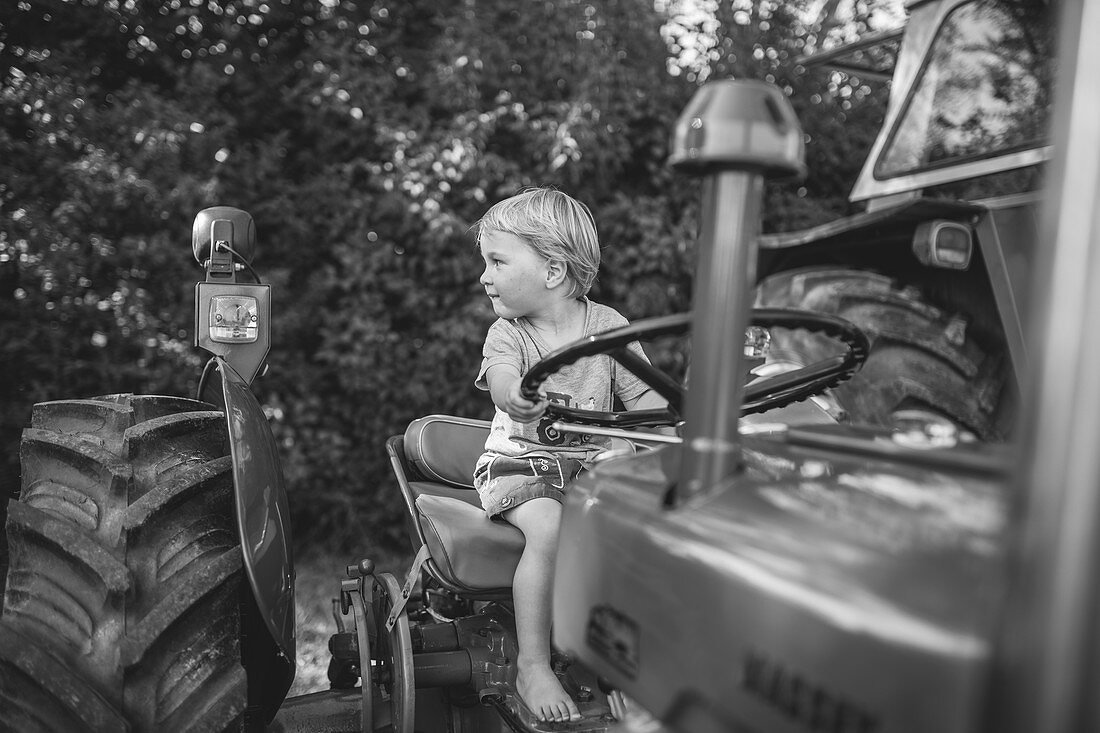 Little boy sits on an old tractor and steers, black and white, Allgäu, Bavaria