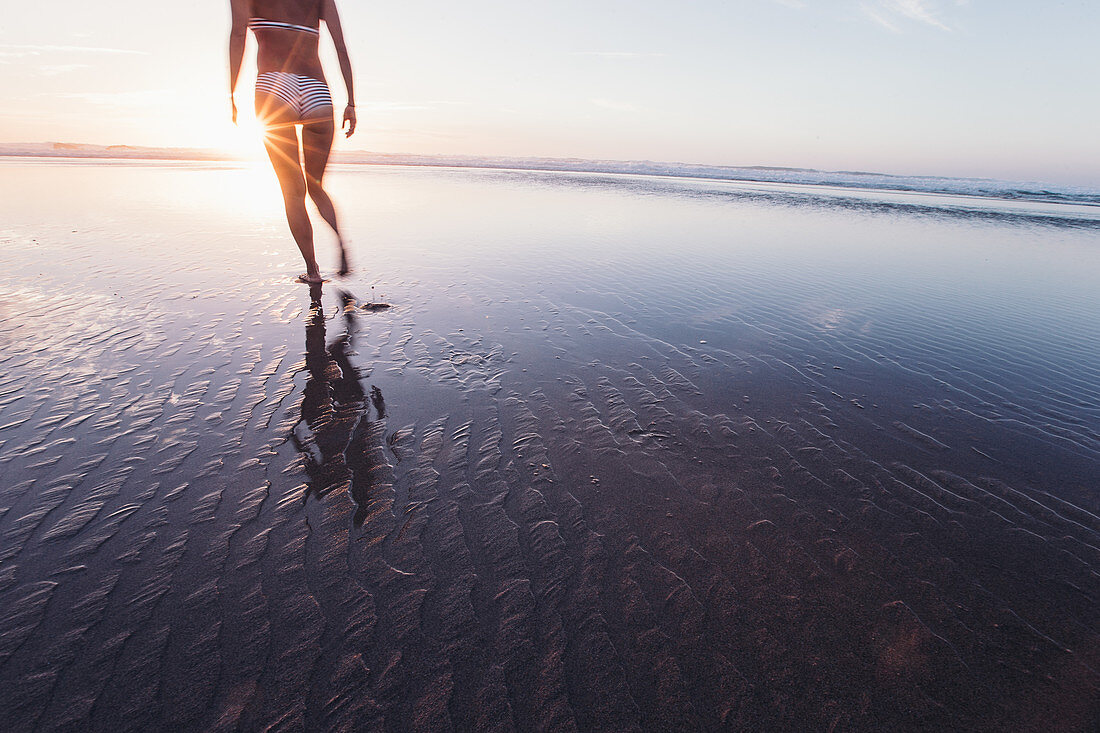 Frau spaziert im Sonnenuntergang am Strand, Portugal