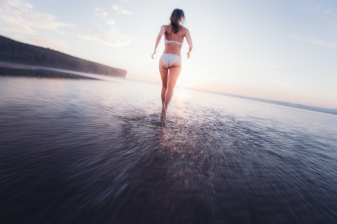 Woman running in bikni over the beach in the evening, Portugal, vacation