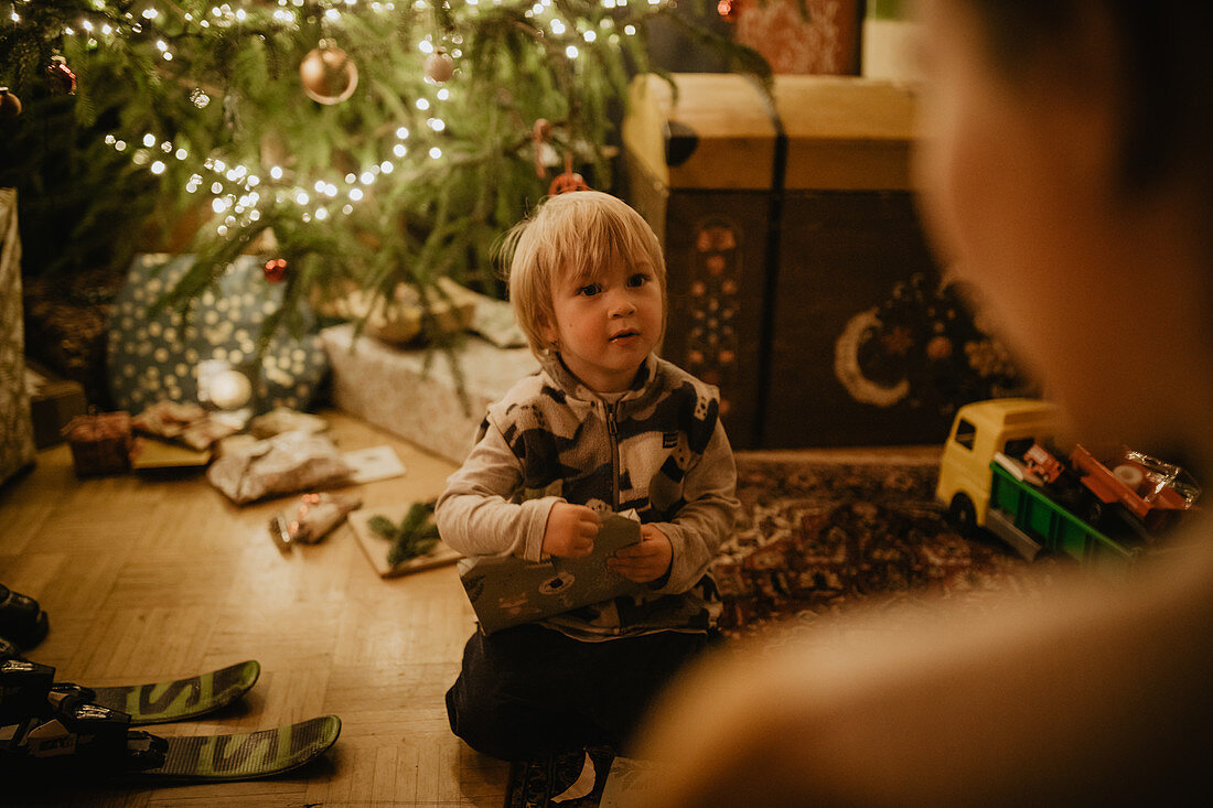 Kleiner Junge packt vorm Christbaum seine Geschenke aus