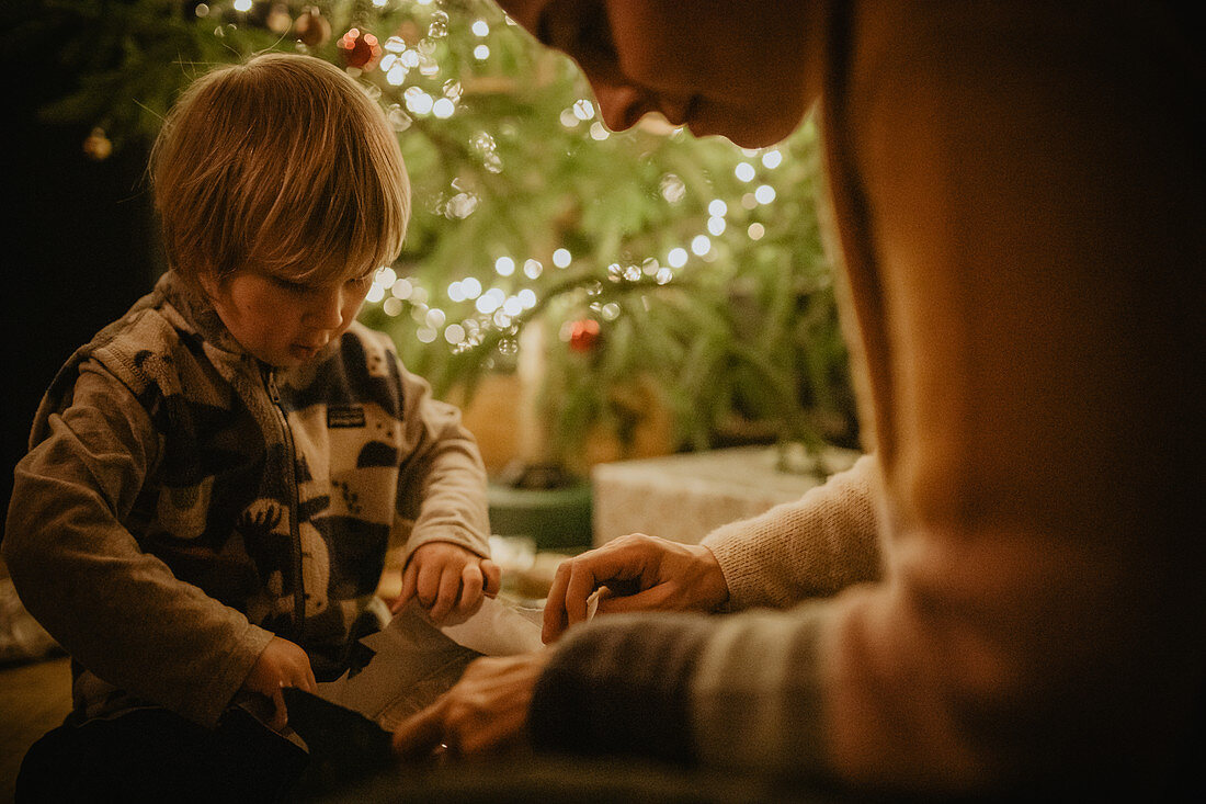 Kleiner Junge packt vorm Christbaum seine Geschenke aus