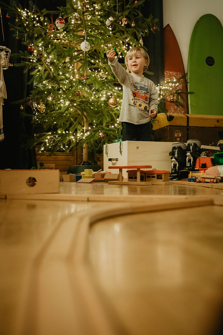 Kleiner Junge spielt mit seinem Holzzug vorm Christbaum