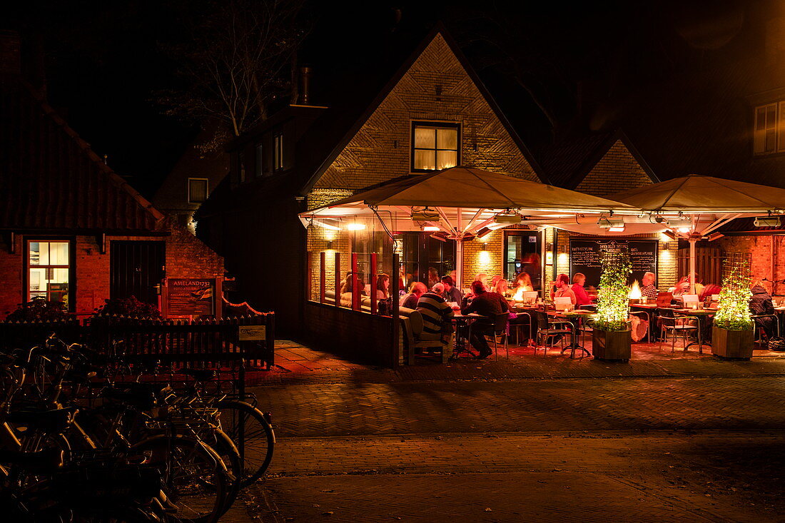 Menschen sitzen draußen und genießen Abendessen im Restaurant Rixt bei Nacht, Nes, Ameland, Westfriesische Inseln, Friesland, Niederlande, Europa