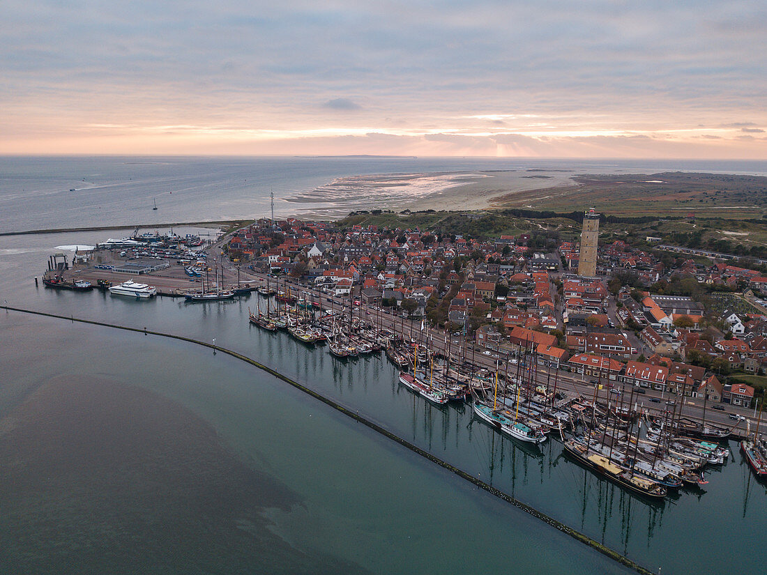 Aerial view of historic flat bottom sailing boats in the harbor of West Terschelling with town and Brandaris lighthouse at sunset, West Terschelling, Terschelling, West Frisian Islands, Friesland, Netherlands, Europe