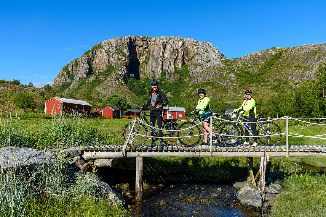 Radfahrer auf kleiner Brücke mit roten Häusern vor Torghattan, Bronnoysund, Norwegen