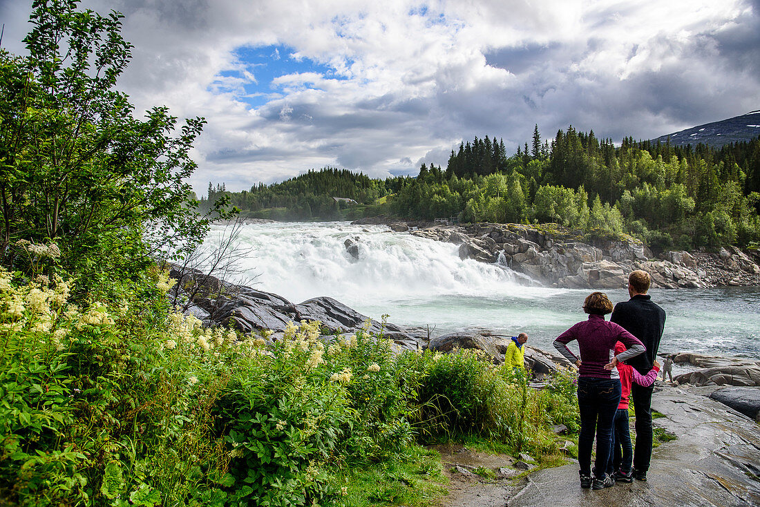 Family gazes at waterfall, The Vefsna River with the Laksfossen waterfall, Norway