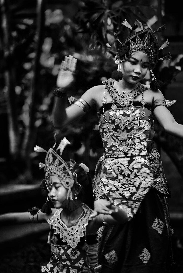 Two young Balinese girls perform a traditional dance in costume at their family compound in Ubud Bali Indonesia.
