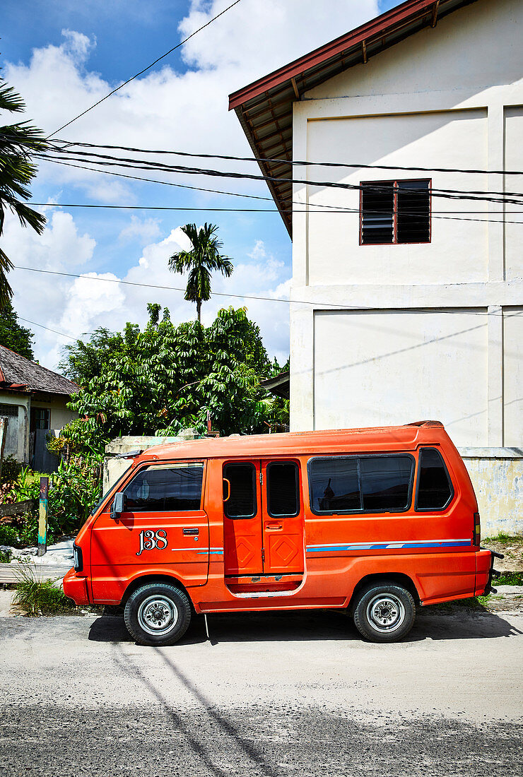 Ein kleines orangefarbenes Taxi parkt am Straßenrand in einer Straße in Palangkaraya, Zentralkalimantan, Borneo, Indonesien