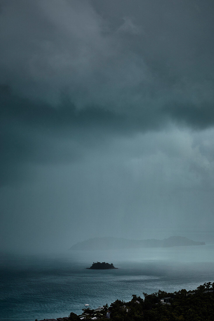 A rainstorm over Plum Pudding Island shot from a lookout on Hamilton Island, Whitsunday Islands, Queensland, Australia.