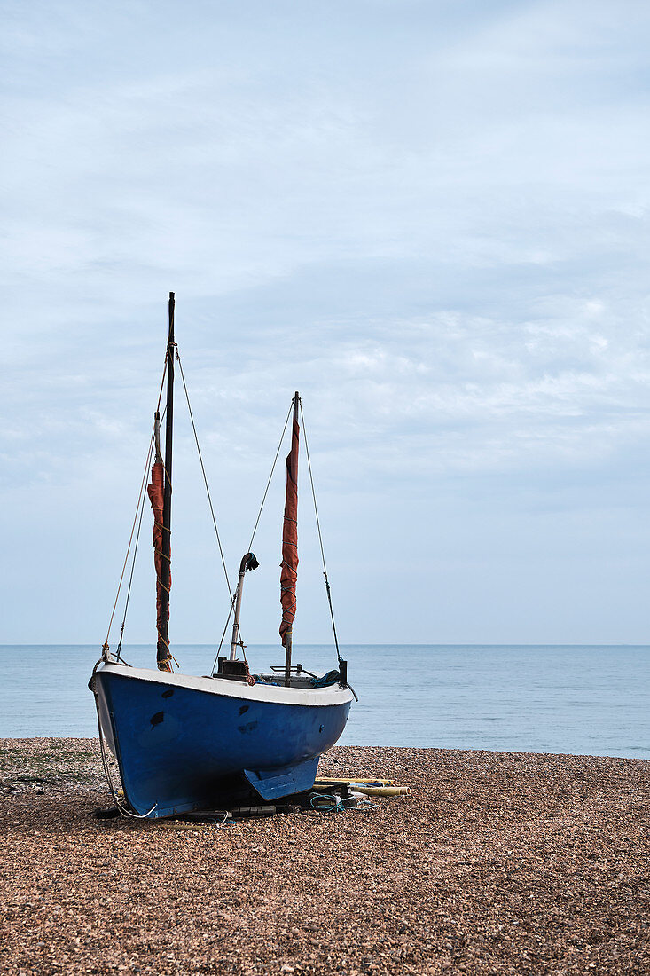 A traditional fishing boat sits on the pebbled sea shore of Rock A Nore beach looking out to the English Channel, Hastings, East Sussex, UK.
