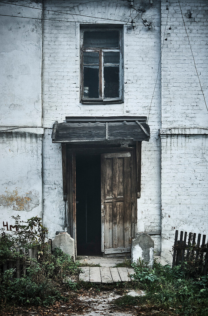 Eine Tür eines alten heruntergekommenen Hauses in einer nebligen Gasse im Morgengrauen in einer kleinen Stadt außerhalb von Moskau, Russland