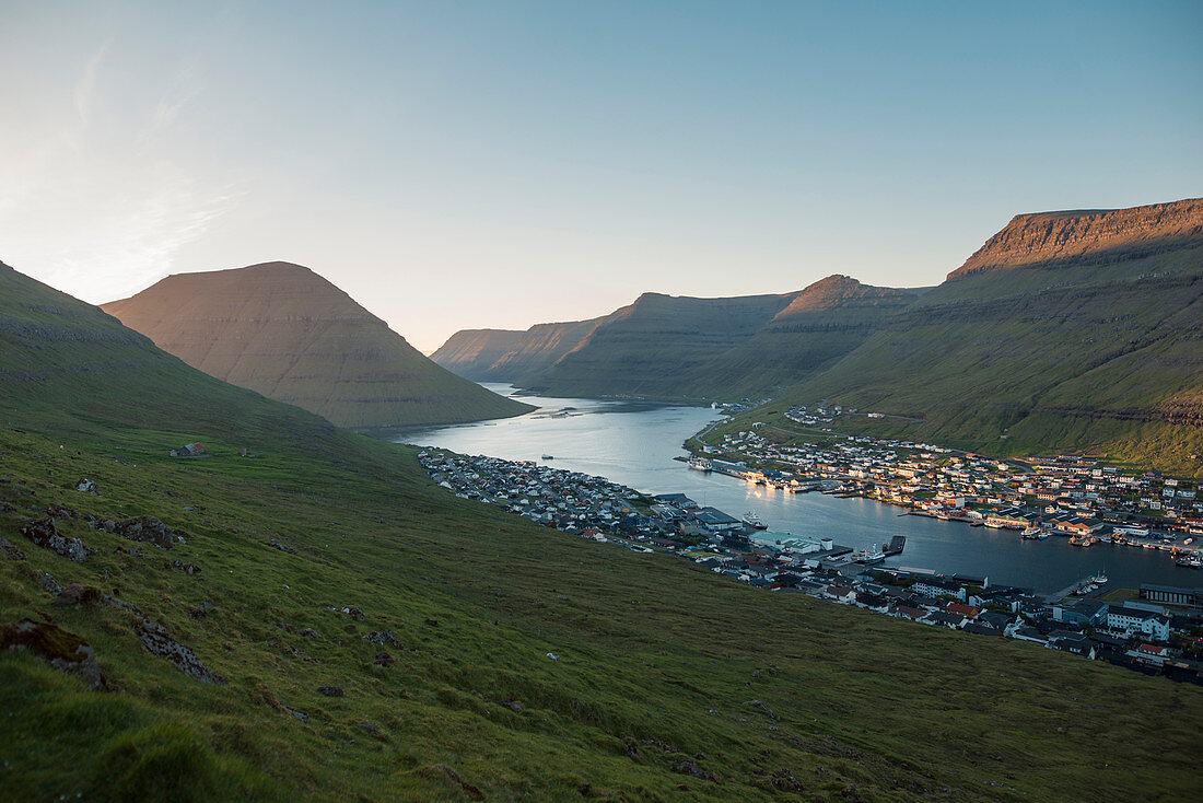 Dänemark, Färöer, Klaksvik, Landschaft mit Bergen und Dorf auf dem Seeweg im Morgengrauen