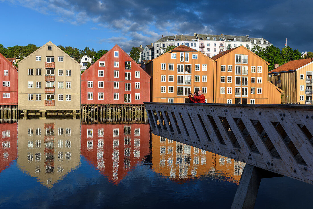 Menschen auf Aussichtsplattform am Fluss Nidelv mit alten Lagerhäusern, Trondheim, Norwegen