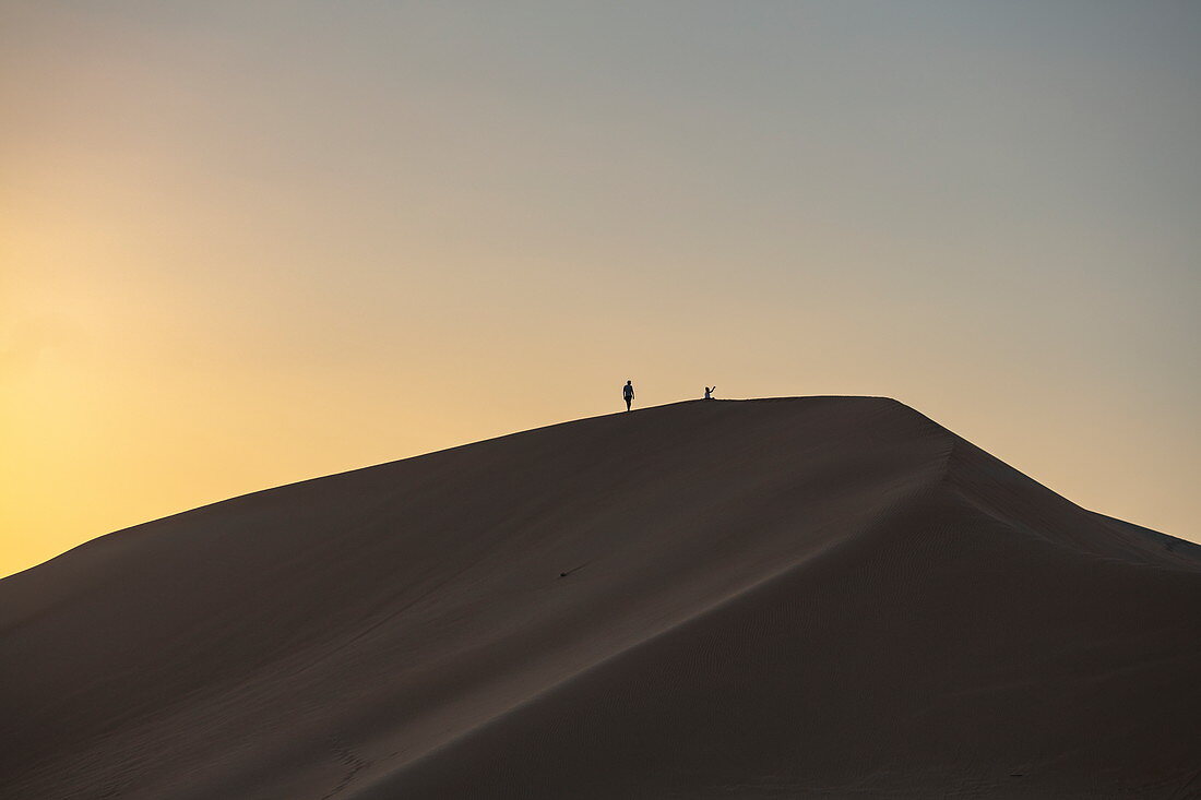 Silhouette of people on sand dune outside Arabian Nights Village desert resort at sunset, Arabian Nights Village, Razeen Area of Al Khatim, Abu Dhabi, United Arab Emirates, Emirates, Middle East