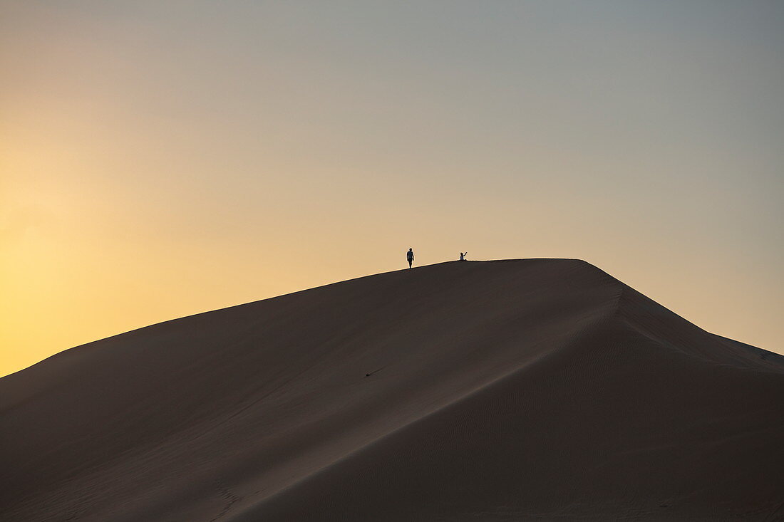 Silhouette von Menschen auf Sanddüne außerhalb Arabian Nights Village Wüstenresort bei Sonnenuntergang, Arabian Nights Village, Razeen Area of Al Khatim, Abu Dhabi, Vereinigte Arabische Emirate, Emirate, Naher Osten