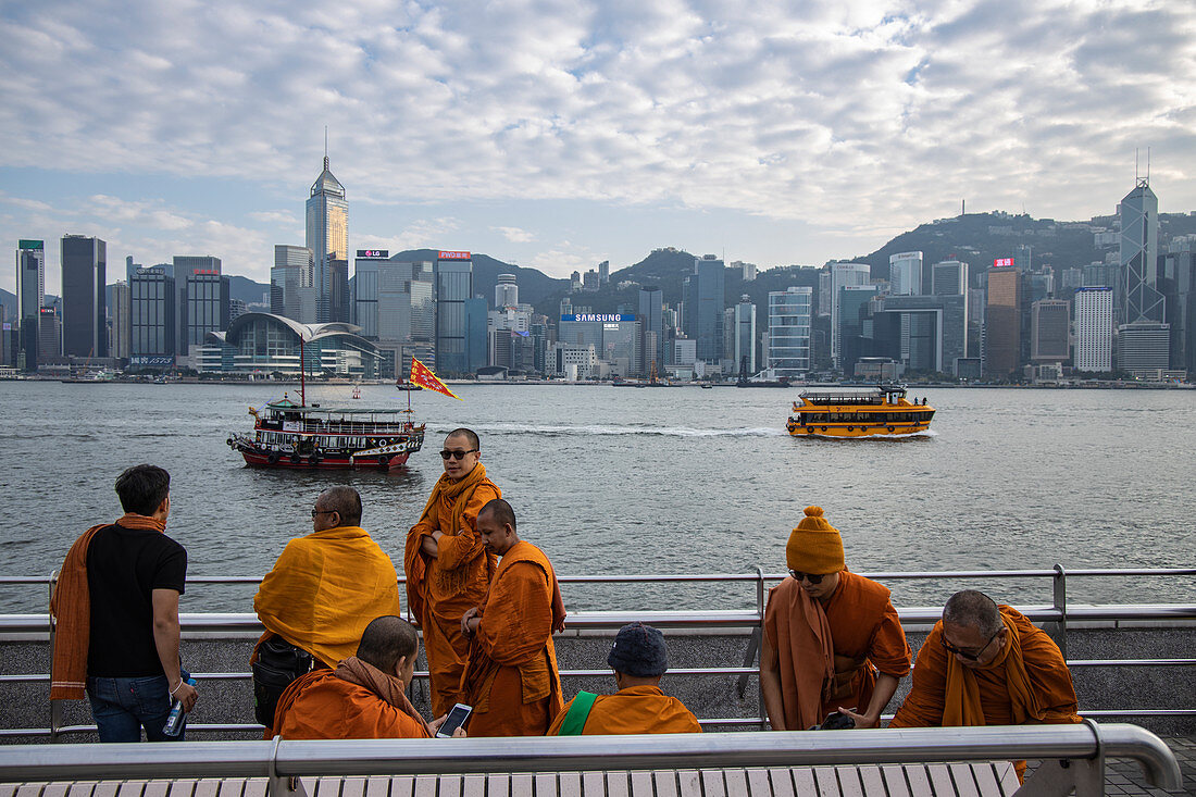 Mönche auf der Tsim Sha Tsui-Seite des Victoria Harbour mit der Skyline von Hongkong in der Ferne, Hongkong, Hongkong, China, Asien