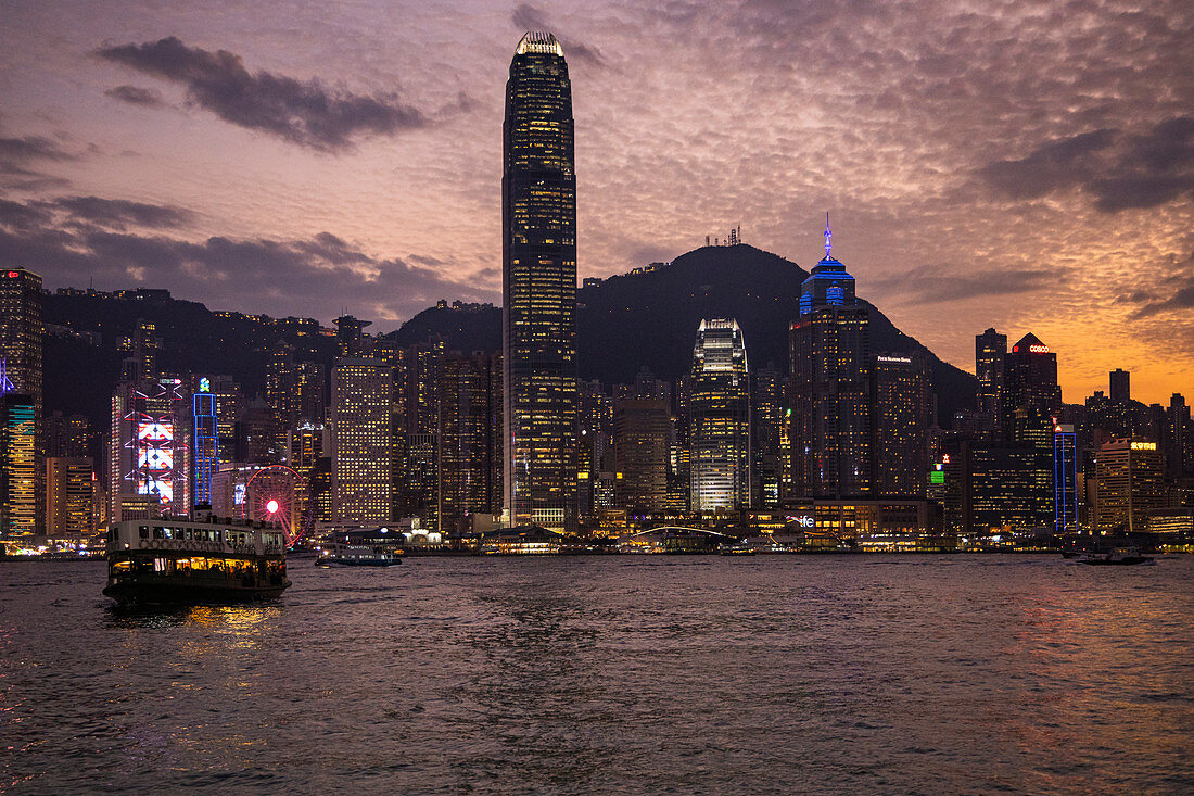 Kowloon Fähre überquert Victoria Harbour mit der Skyline von Hongkong in der Ferne bei Sonnenuntergang, Hongkong, Hongkong, China, Asien