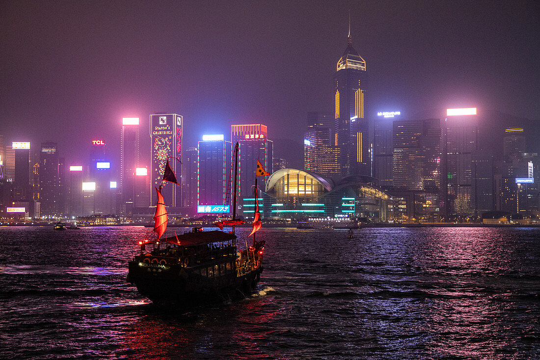Traditionelle Dschunke die als Touristen Sightseeing-Boot dient im Victoria Harbour mit Skyline von Hongkong dahinter bei Nacht, Hongkong, Hongkong, China, Asien