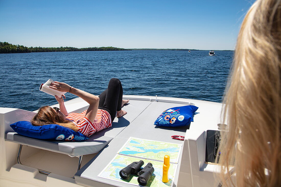 Junge Frau entspannt sich auf dem Sonnendeck von einem Le Boat Horizon Hausboot und liest ein Buch, Lower Rideau Lake, Ontario, Kanada, Nordamerika